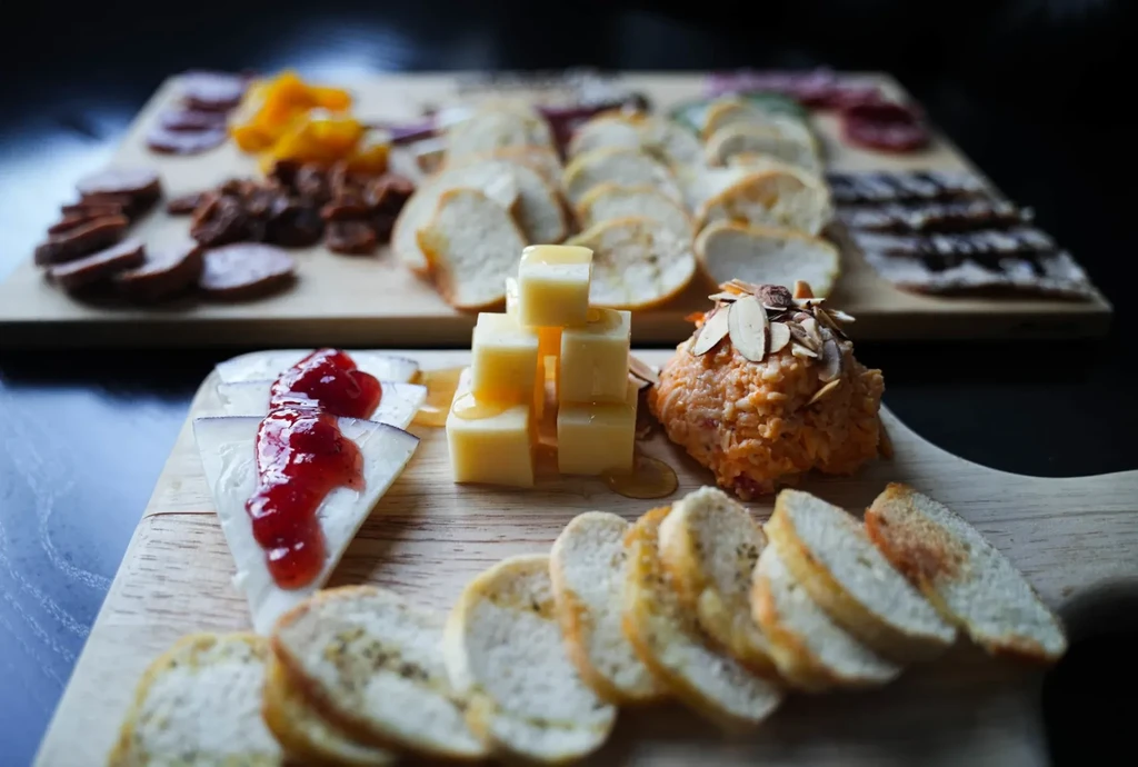 Two wooden boards laden with cheese, bread, jam, honey, and charcuterie.