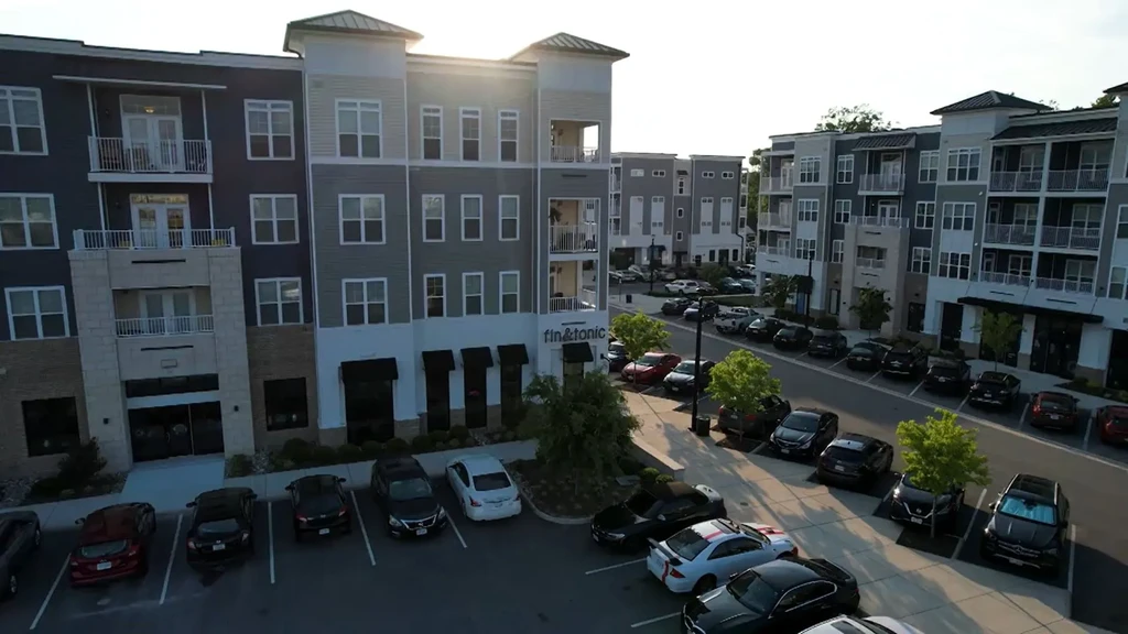 Modern mixed-use development with street, parked cars, and "fin&tonic" sign.
