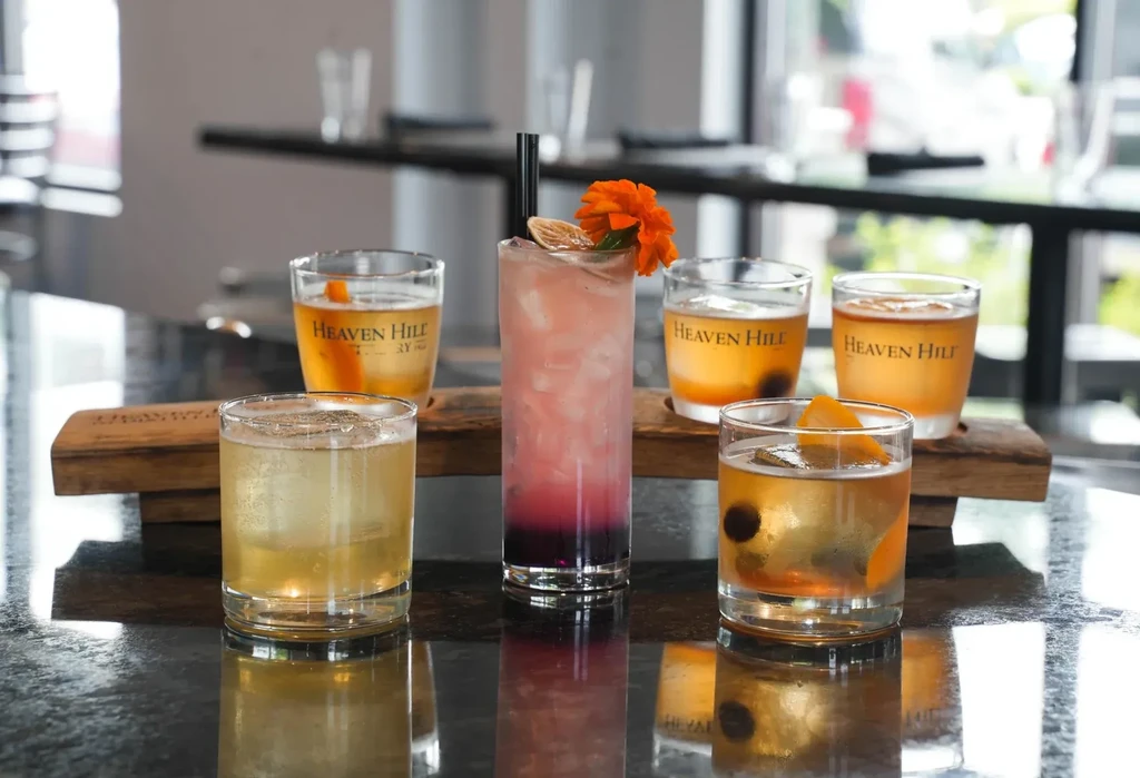 Heaven Hill spirit samples and a layered cocktail on a dark bar.
