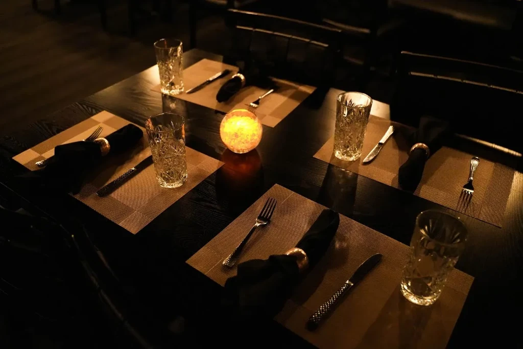 Dimly lit restaurant with elegantly set tables and a glowing orange light.