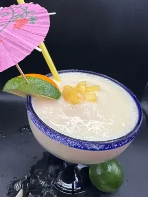 Frozen off-white cocktail, pineapple, lime, orange, straw, umbrella.