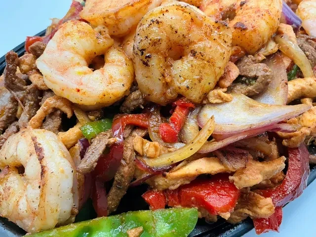 Close-up of cooked shrimp, beef, peppers, and onions stir-fry.