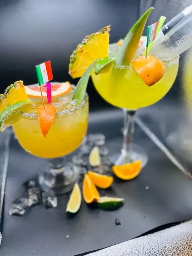Two elaborately garnished cocktails in large glasses against a dark background.