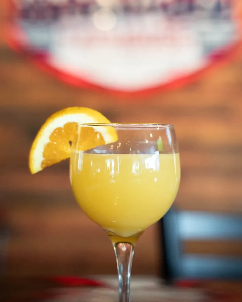 Wine glass filled with orange drink, garnished with an orange slice.