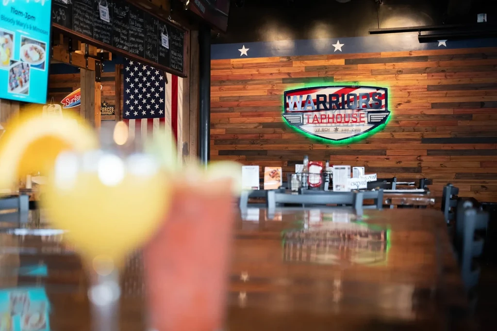 Warriors Taphouse interior with drinks, American flag, and neon sign.