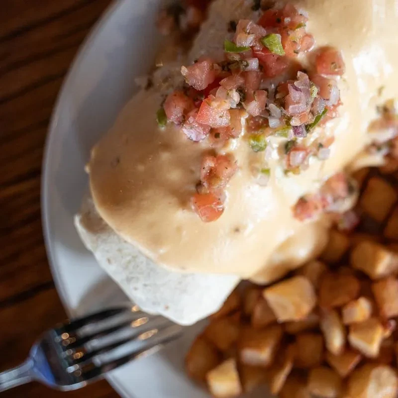 A sauced burrito topped with pico de gallo, alongside roasted potatoes.