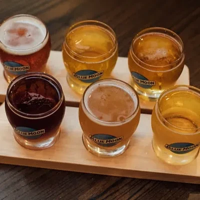 Six Blue Moon beers on a wooden flight paddle, varied colors.