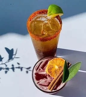 Two distinct cocktails: amber with lime, dark red with orange and spices.