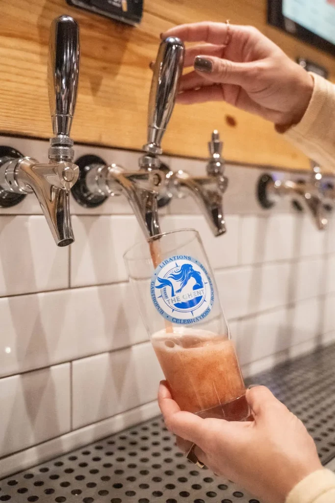 Hands pour foamy reddish-brown drink from tap into Libations Gastropub glass.