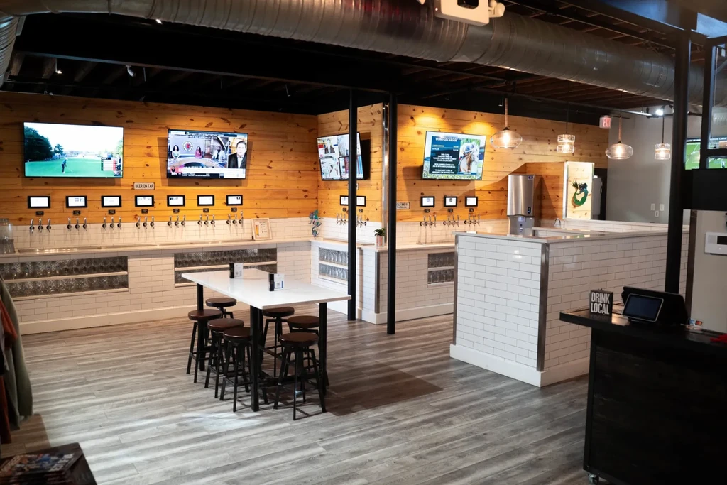 Self-pour taproom interior with wood, tile, digital taps, and flat-screen TVs.