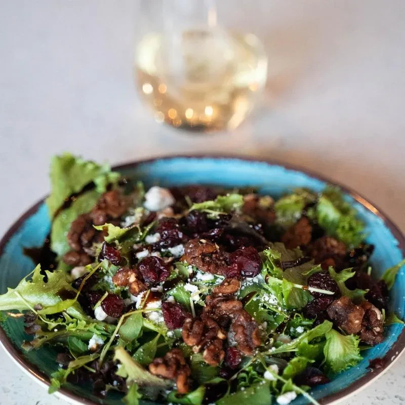 Salad with greens, cranberries, walnuts, and crumbled cheese in blue bowl.