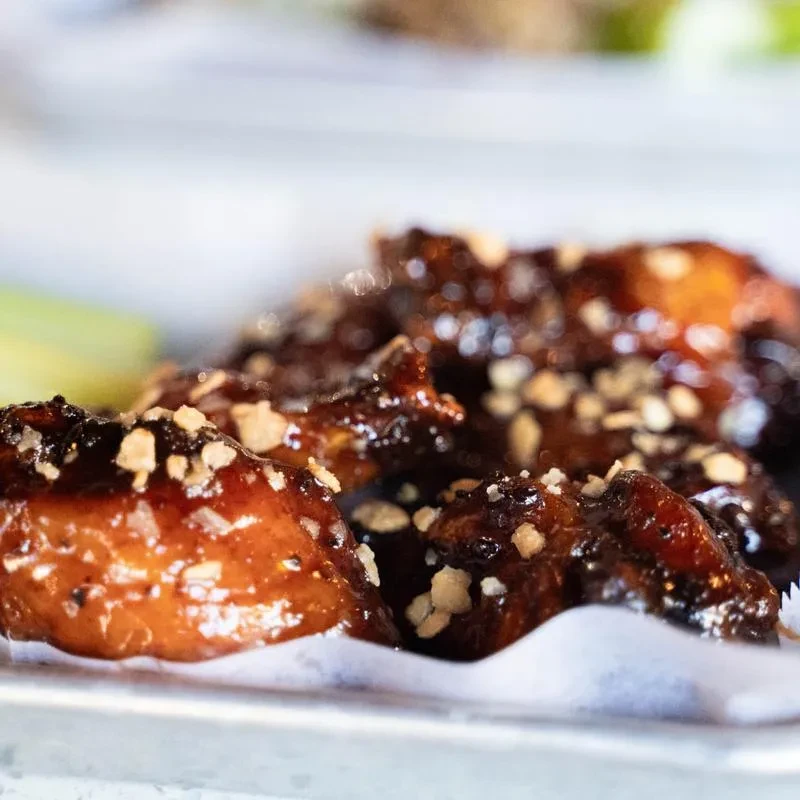Glossy chicken wings with dark sauce and light crumbles on a tray.