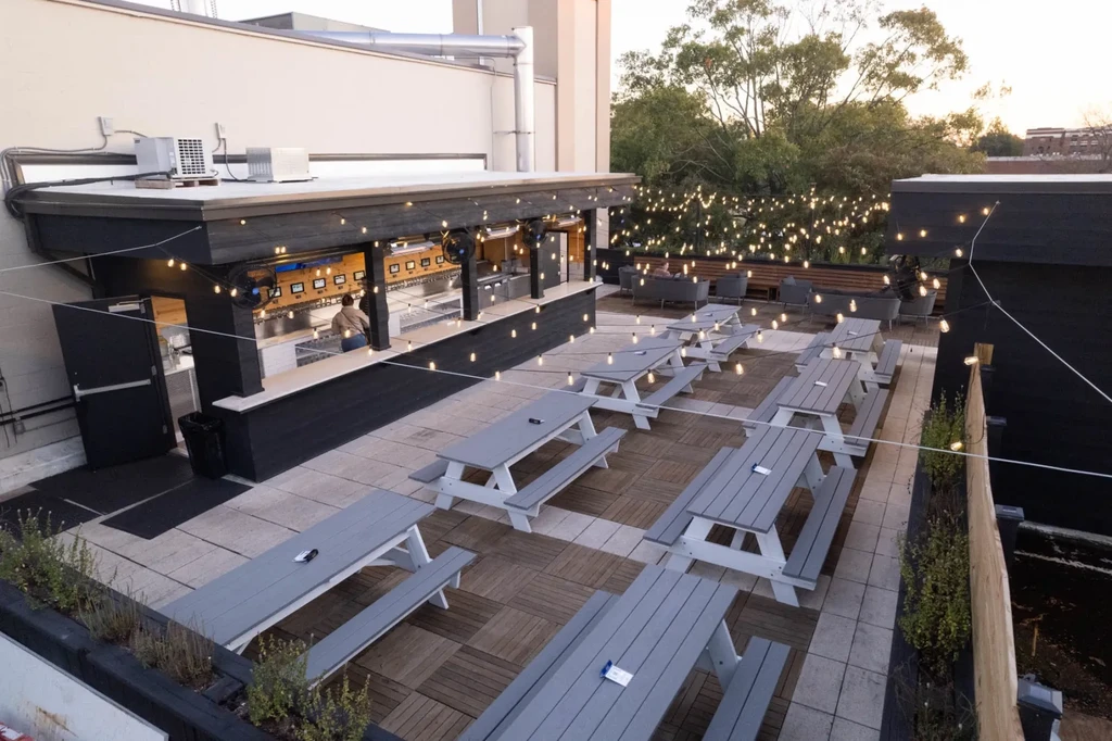 Rooftop bar with picnic tables, lounge seating, and illuminated string lights.