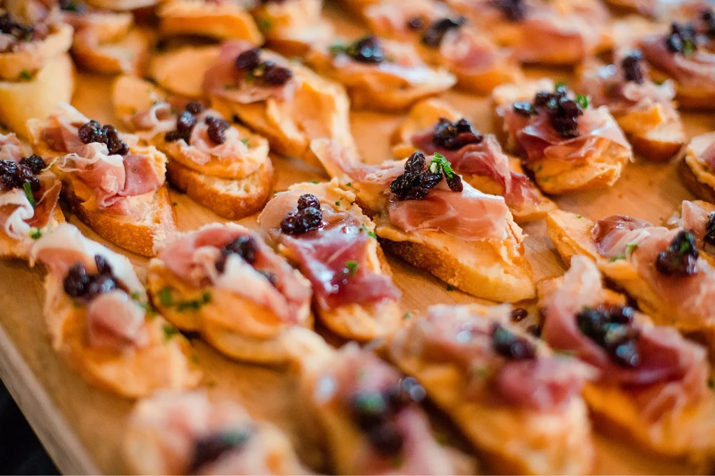 Many crostini with cured meat, creamy spread, and berry compote.