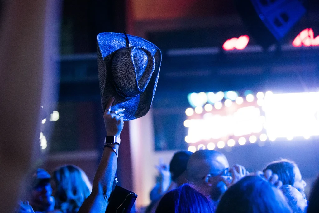 Raised arm, cowboy hat, rings, smartwatch in dark concert venue.