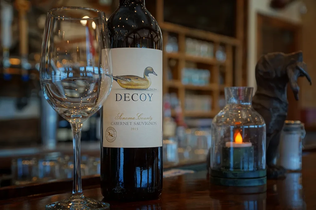 Wine bottle with duck label, empty glass, and lit lantern on bar.