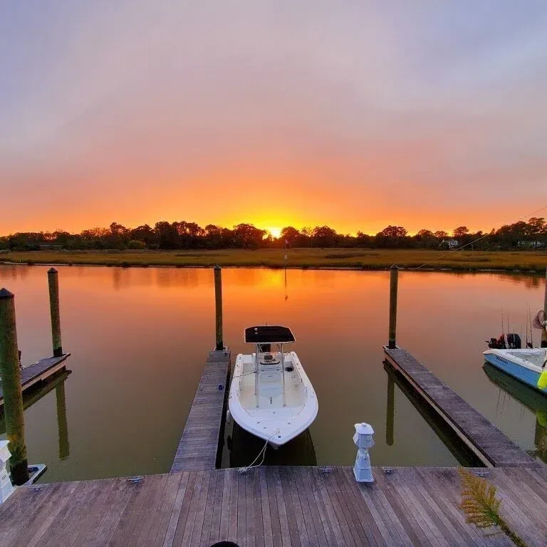 Vibrant sunset reflects on water, boat moored at wooden dock.