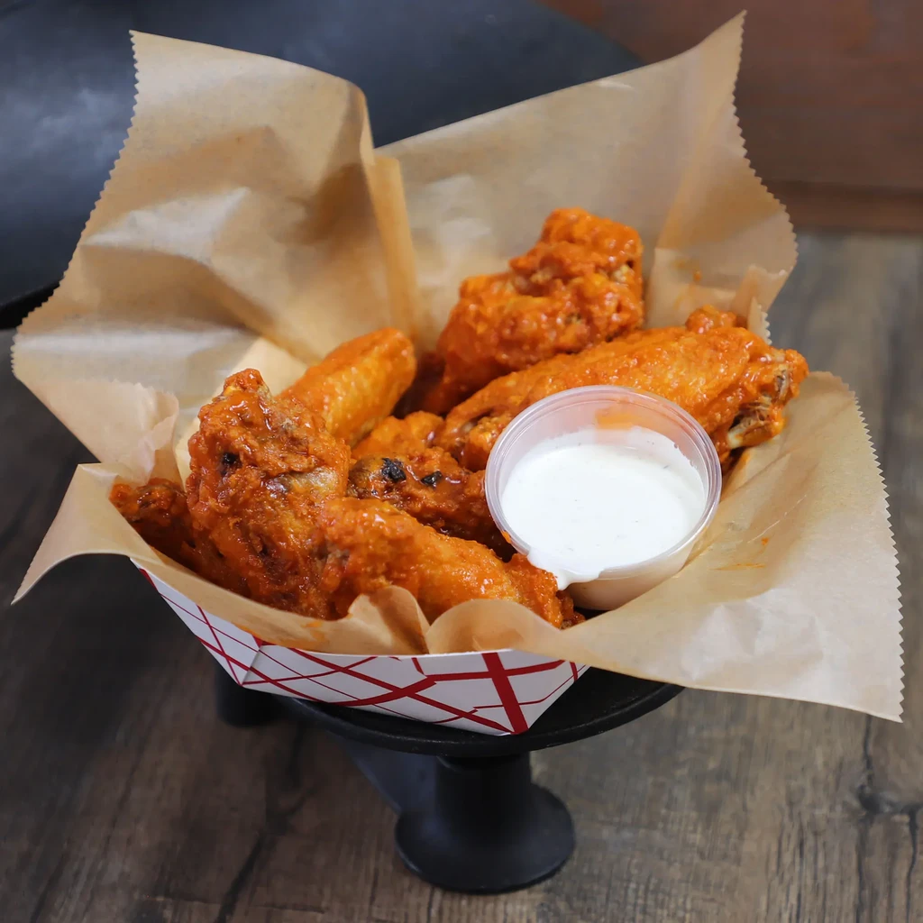 Buffalo chicken wings in a checkered paper boat with dipping sauce.