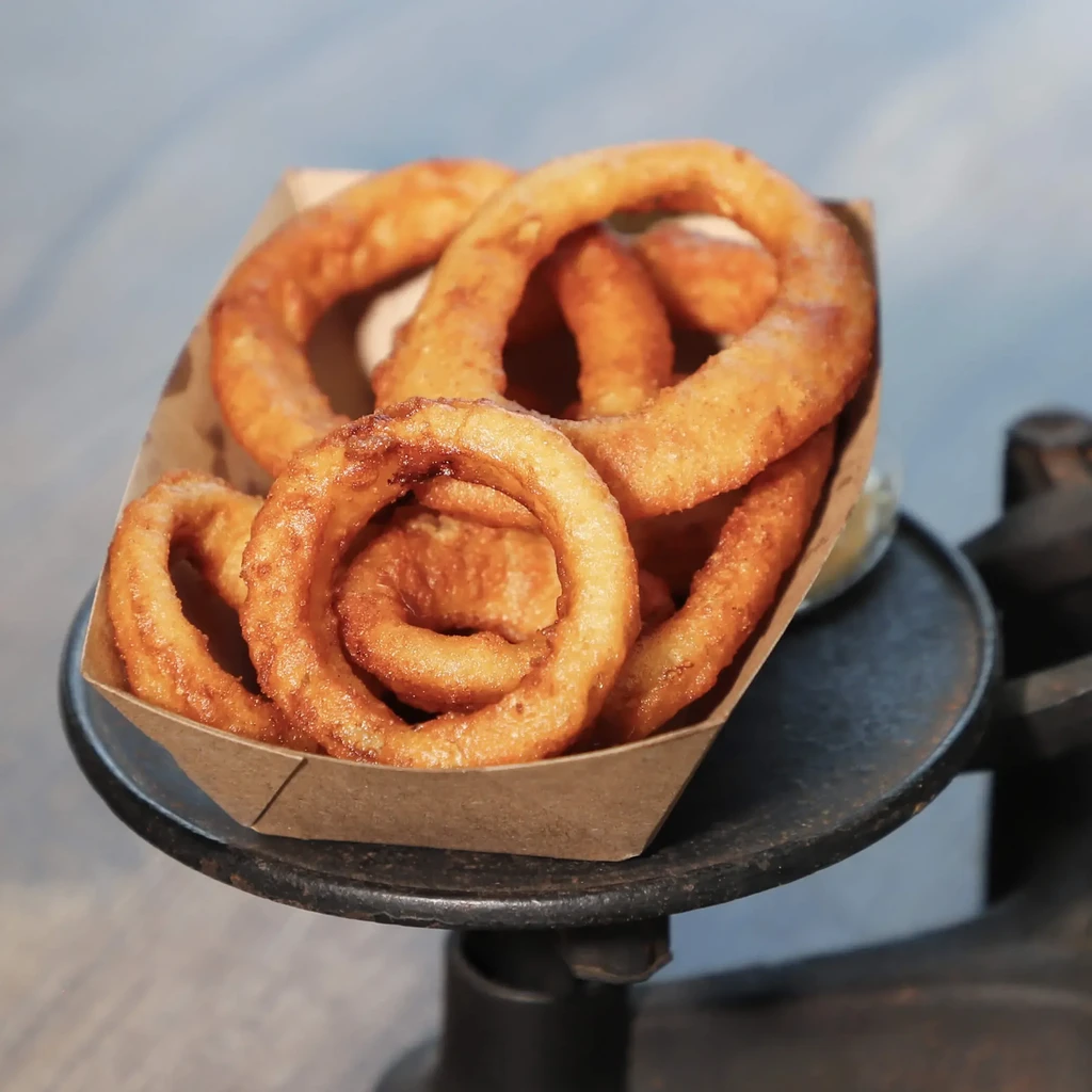 Crispy golden-brown onion rings in a cardboard boat on a rustic metal stand.