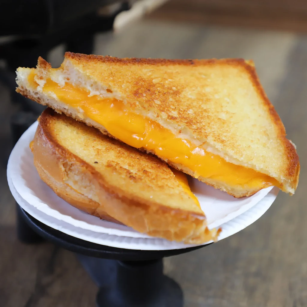 Diagonal grilled cheese sandwich with gooey orange cheese on paper plate.