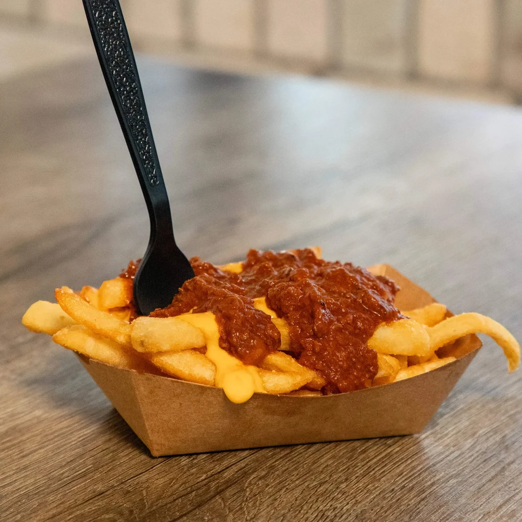 Chunky chili cheese fries in a brown tray with an upright fork.