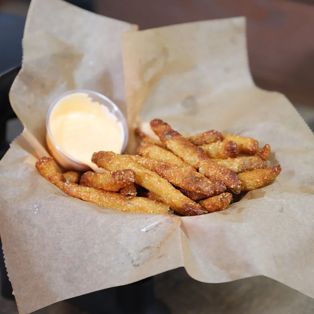 Basket of golden deep-fried green beans/okra with creamy dipping sauce.