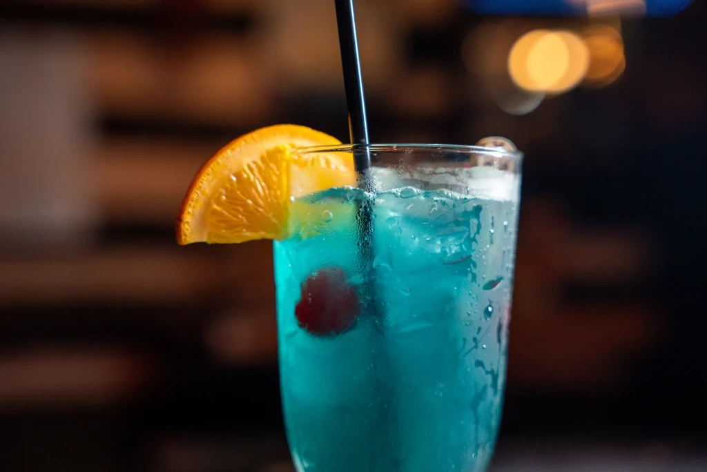 Frosty blue cocktail with orange, cherry, and a black straw.