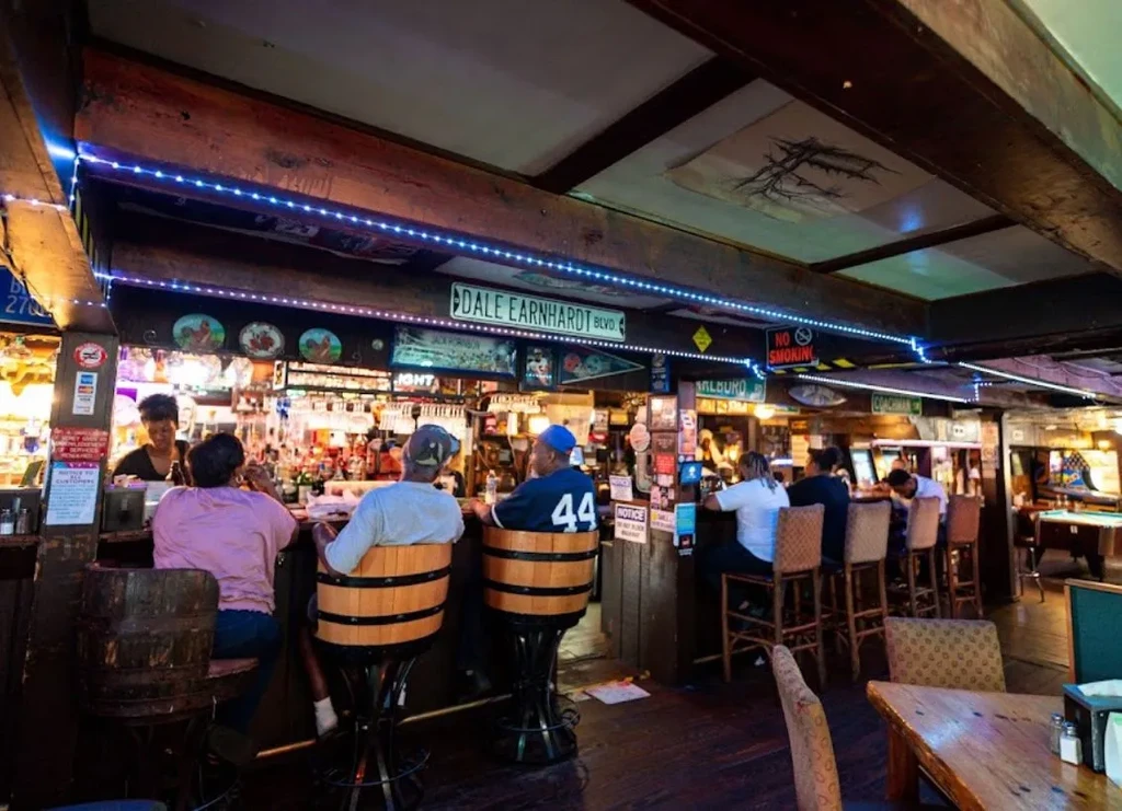Rustic bar interior with patrons, glowing counter, and street signs.