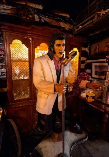 Life-size Elvis Presley statue holding microphone on guitar base.