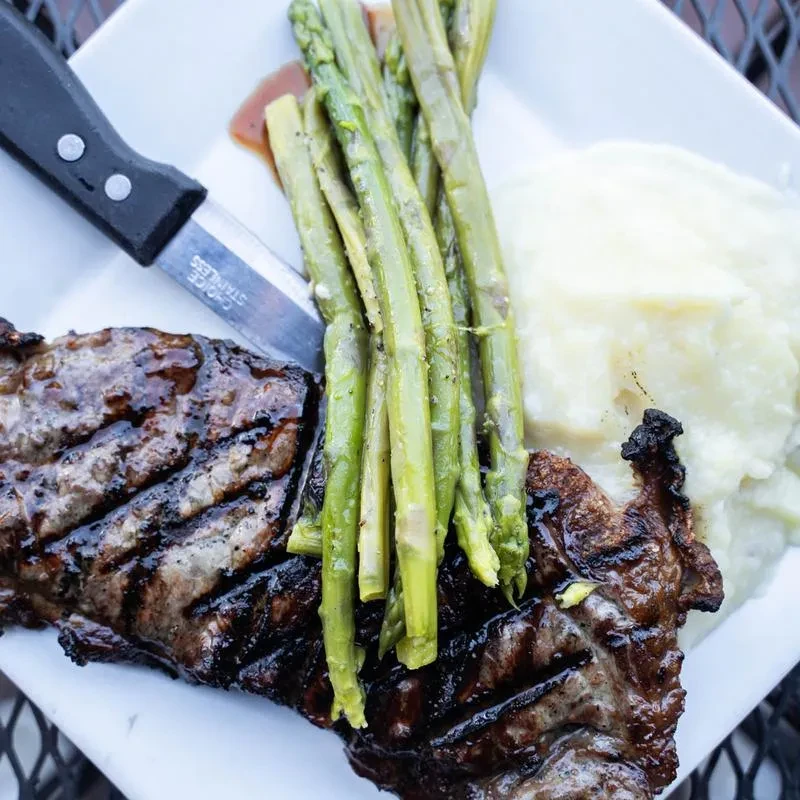 Grilled steak, asparagus, mashed potatoes, and a knife on a plate.