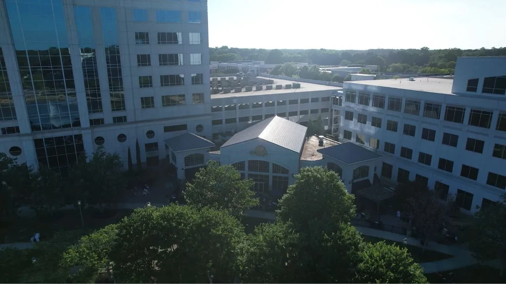 Elevated view of a modern complex with gabled building, offices, and greenery.