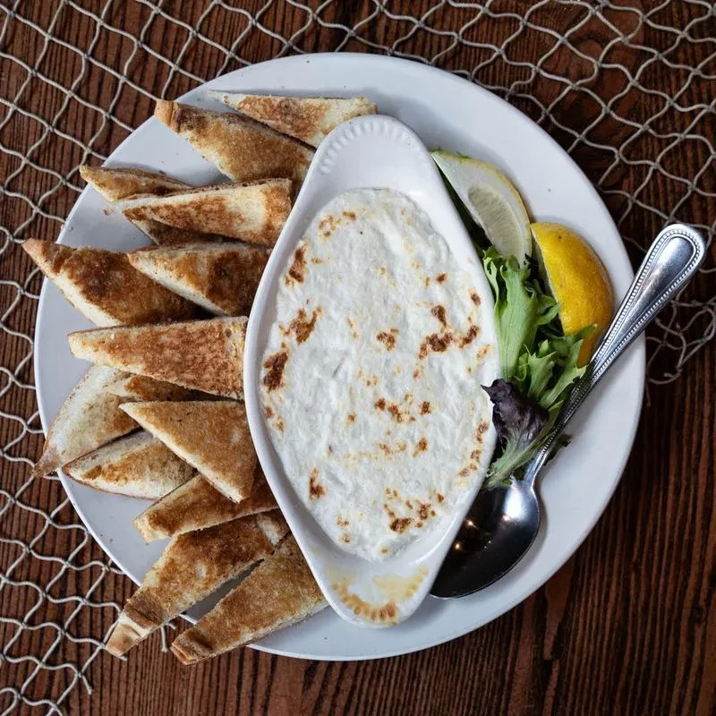 Creamy dip, toasted bread, lemon, and lettuce on a white plate.