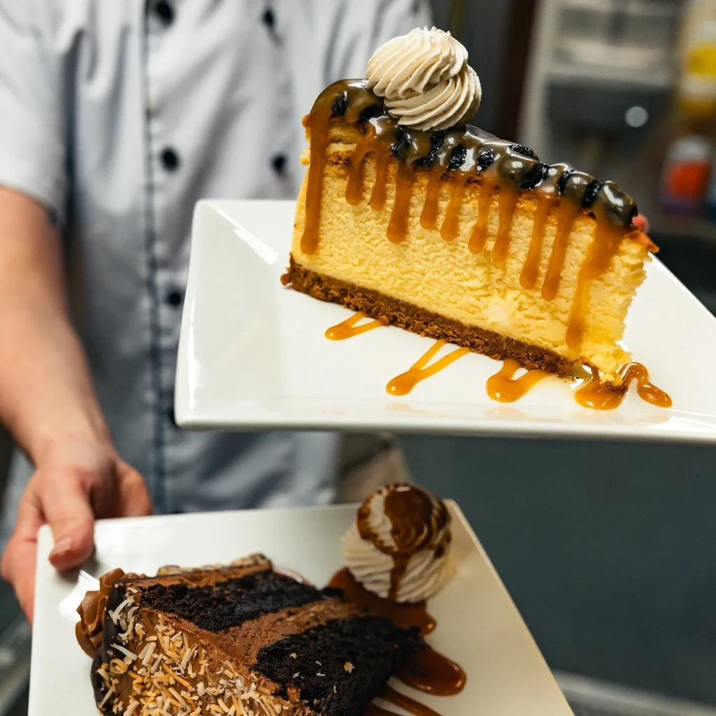 Chef holds two dessert slices: cheesecake with caramel, chocolate cake.