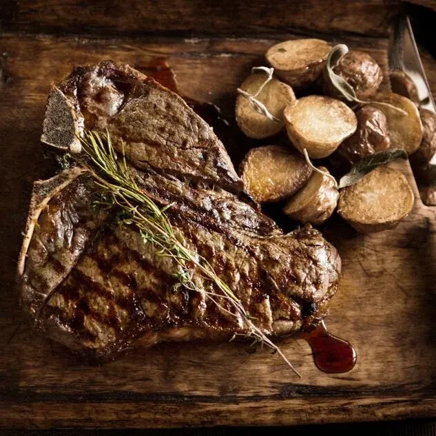 Medium-rare T-bone steak, grill marks, rosemary, roasted potatoes.