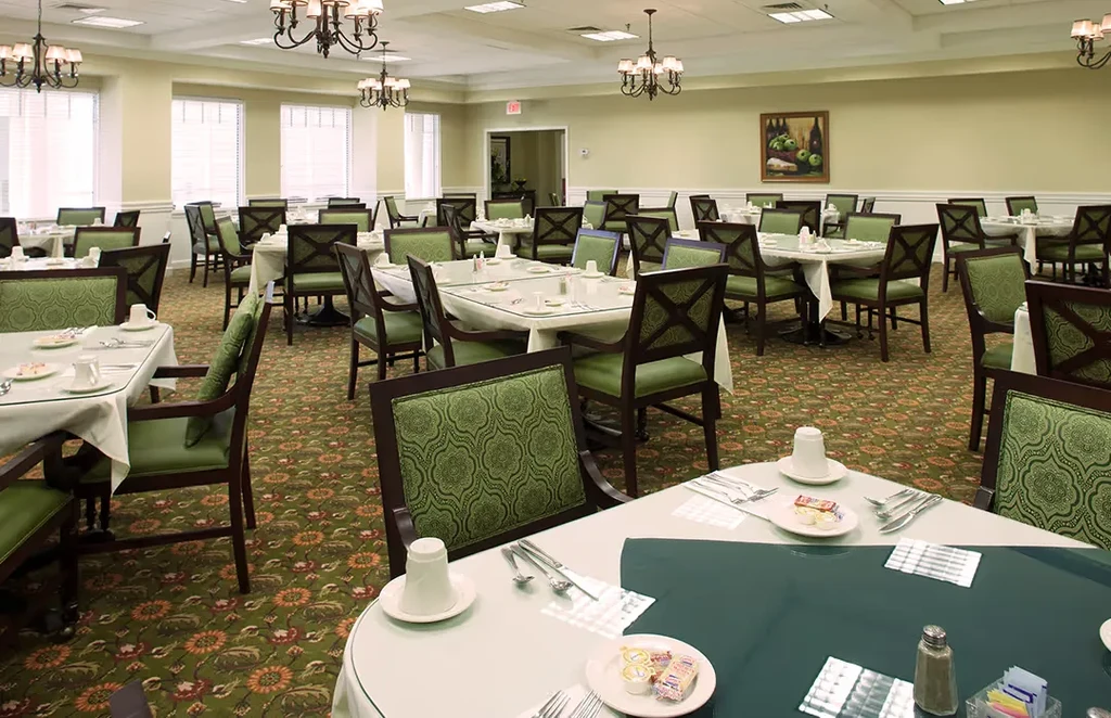 Brightly lit, empty dining room with set tables and green carpet.