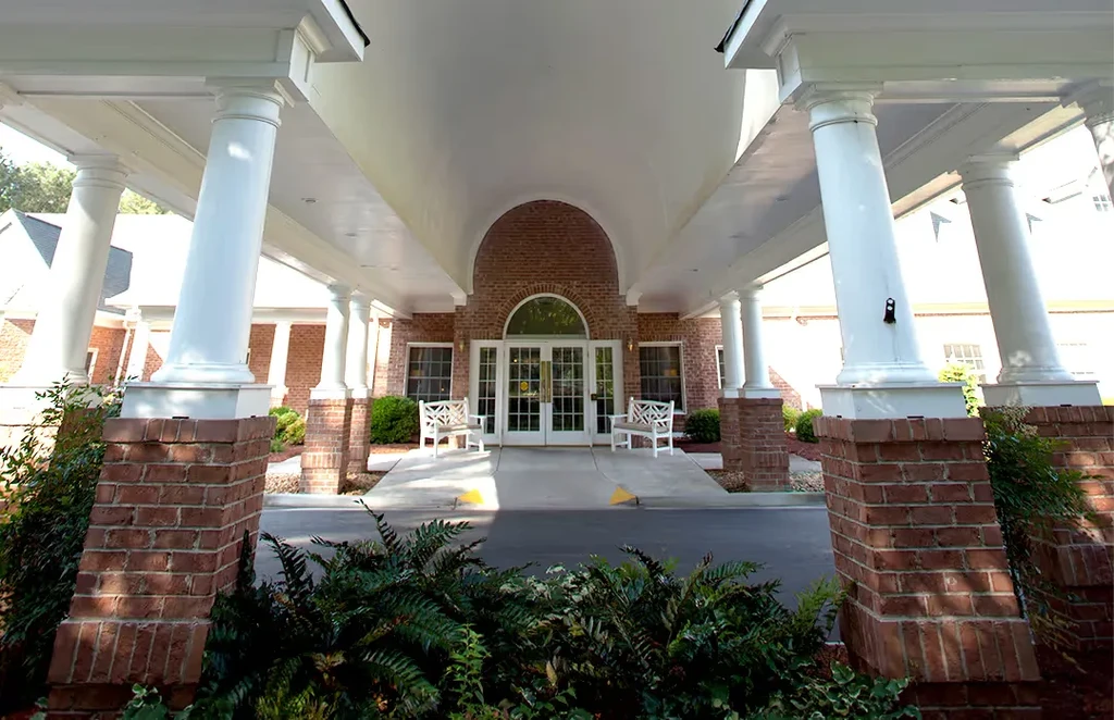 Symmetrical red brick building entrance with white portico and green plants.
