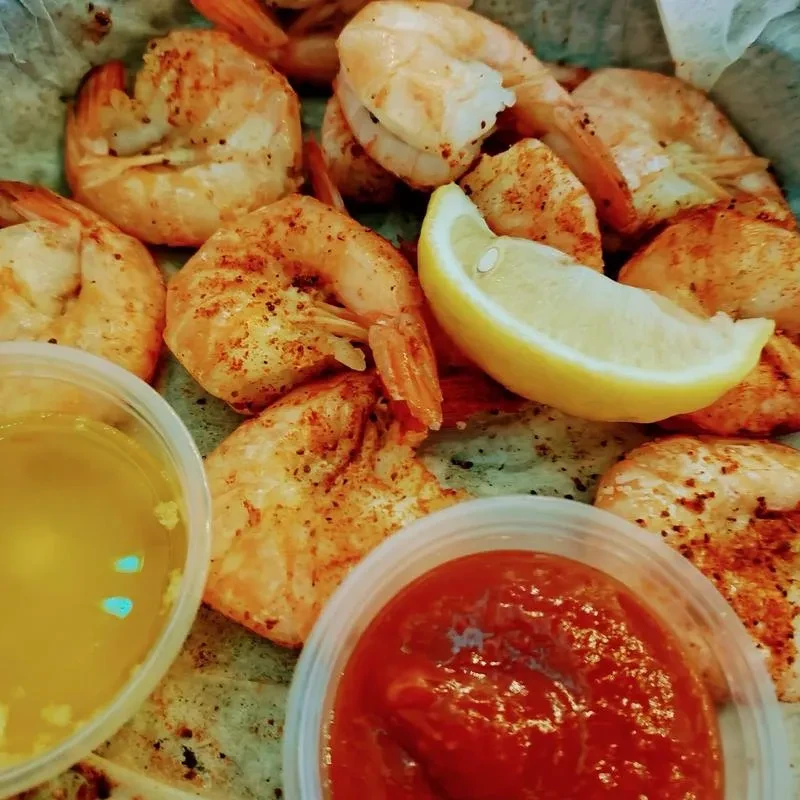 Close-up of seasoned cooked shrimp with lemon, butter, and cocktail sauce.