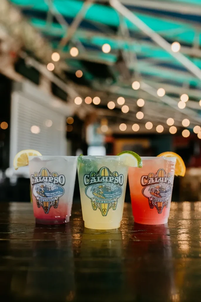 Three branded, colorful drinks with citrus garnishes on a dark table.