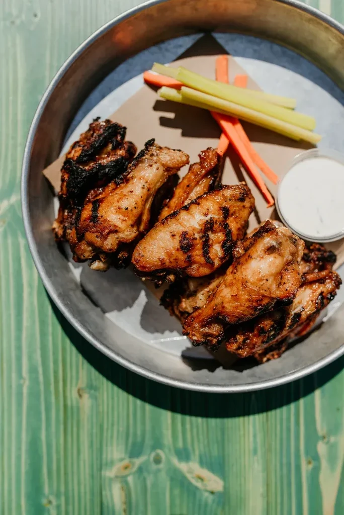 Grilled chicken wings, celery, carrots, and dipping sauce in a metal pan.
