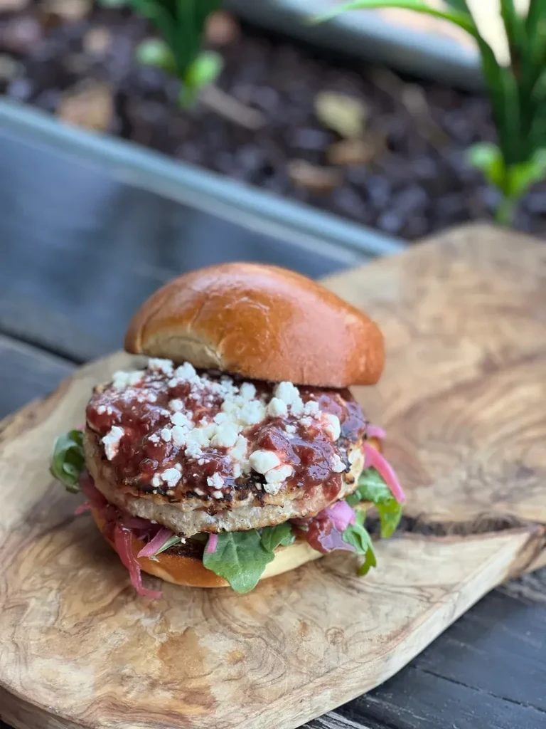 Gourmet burger with dark red sauce and white cheese on olive wood board.