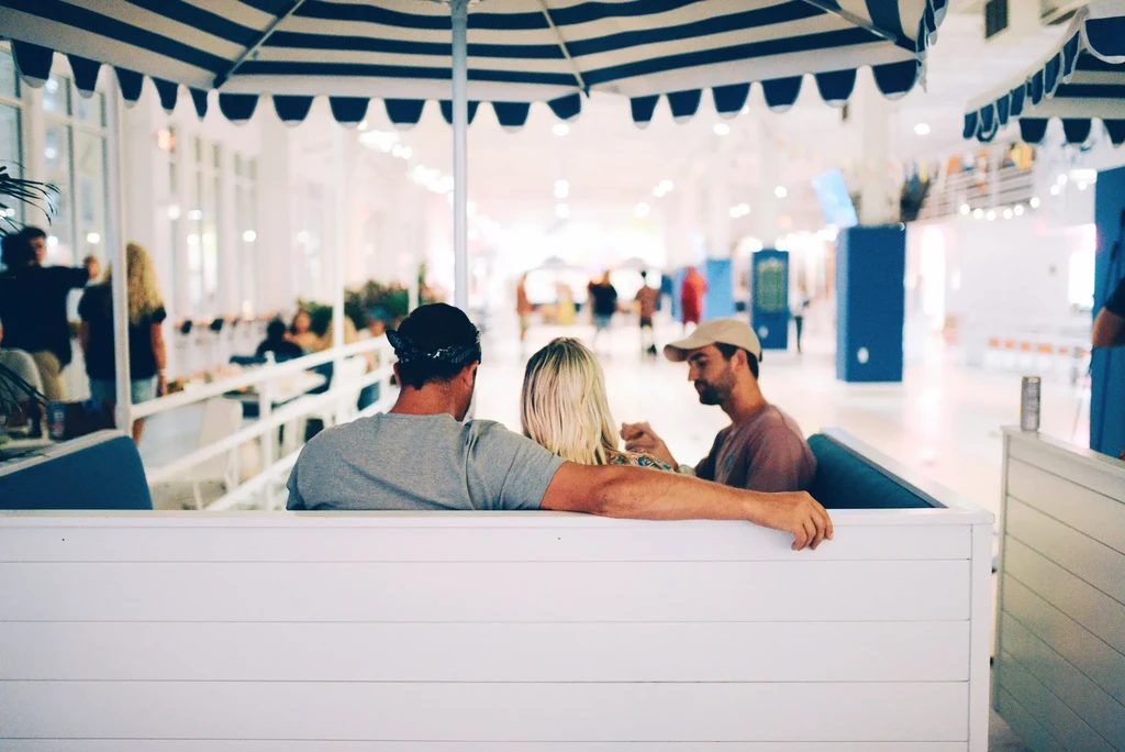 Three people relaxing in a booth under a blue-striped awning.