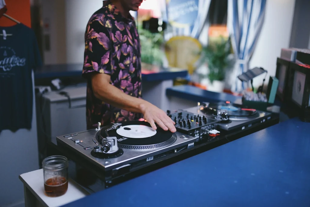 DJ in floral shirt operating turntables and mixing console.