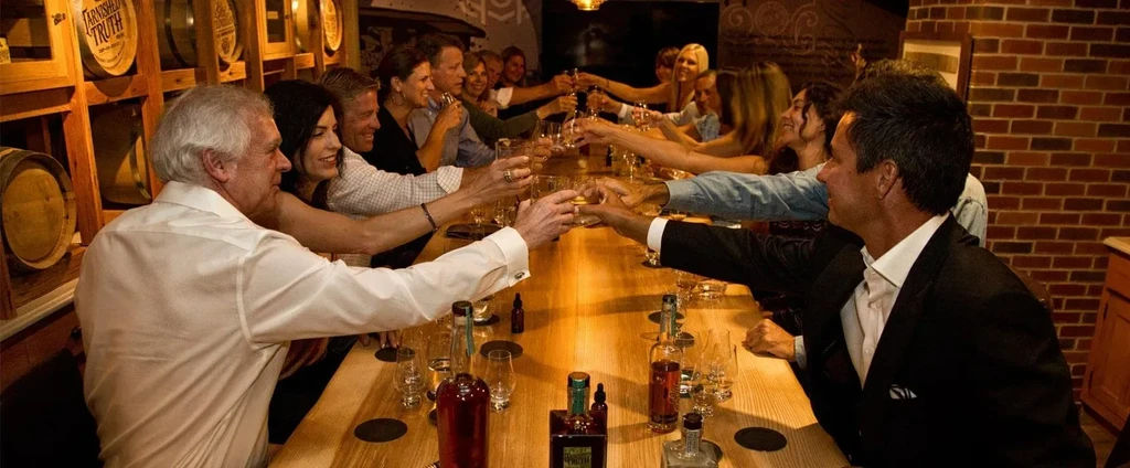 Diverse group clinking glasses in a distillery tasting room.