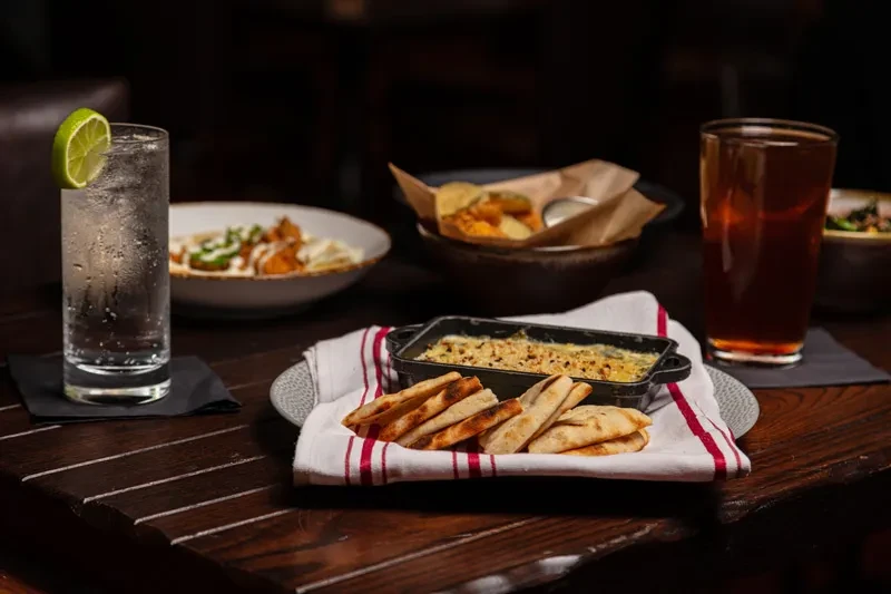 Creamy gratin, flatbread, and drinks on a dark wooden table.