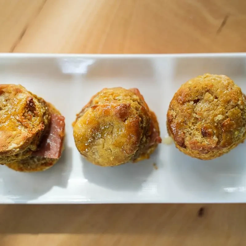 Three golden-brown pastries, one split to reveal ham, on a white plate.