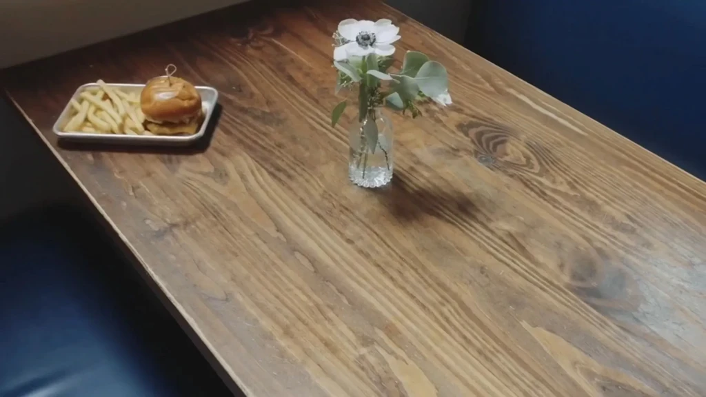 Top-down view: hamburger, fries, and white anemone on wooden table.