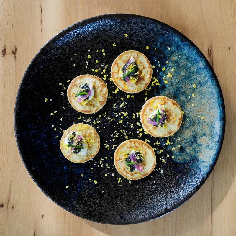 Five blinis with cream, caviar, chives, red onion, and lemon zest.
