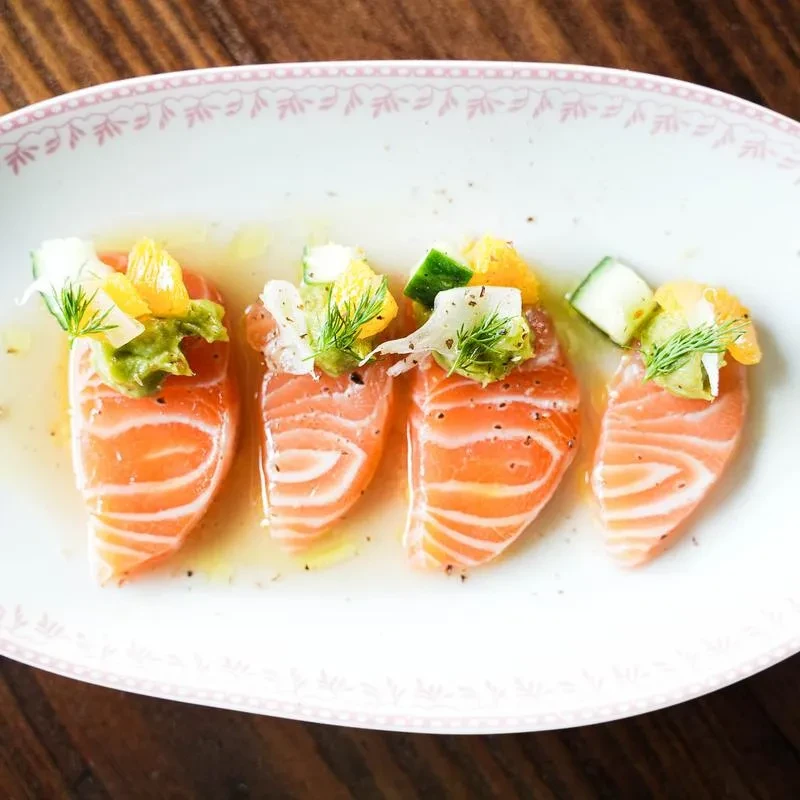 Four raw salmon slices, garnished with citrus, cucumber, and dill.