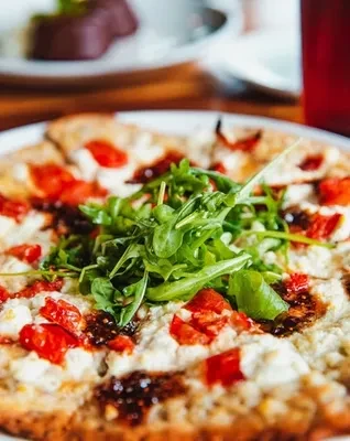 Thin-crust pizza with white cheese, tomatoes, arugula, and balsamic glaze.
