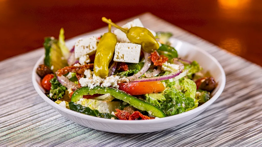 Vibrant Greek salad in a white bowl with feta, olives, and pepperoncini.